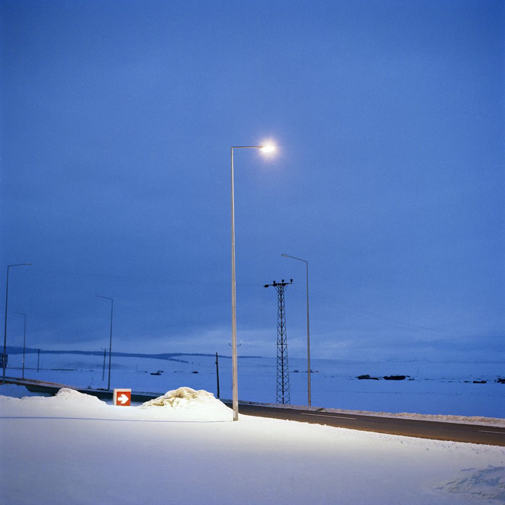 A photo of a street light on a snow covered road.