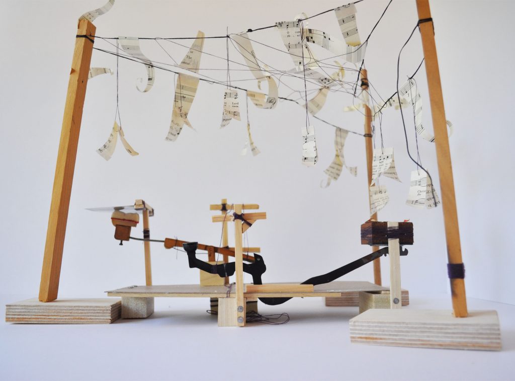 A wooden model featuring threads and music sheets suspended from it created by a student in the STUDIO FIRST program