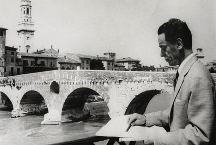An old black and white photo of Gazzola writing near a bridge.