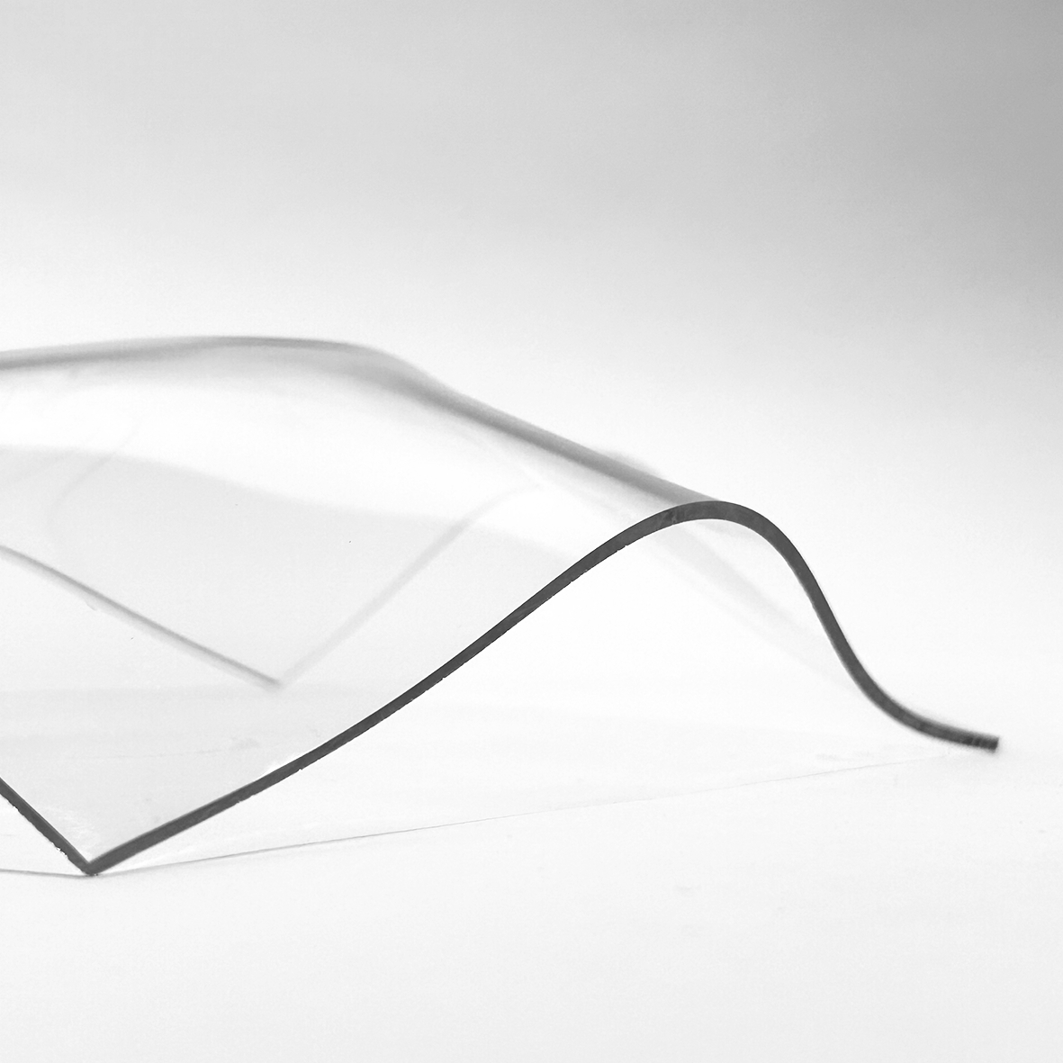 a black and white photograph showcasing a close-up of a thin, undulating piece of glass, creating a smooth wave-like form.