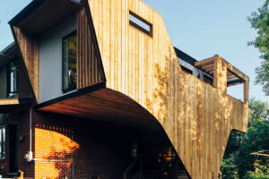 Modern house extension with angled wooden cladding and large overhang, contrasting with the original brick structure below