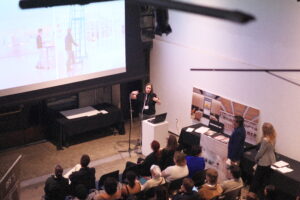 Presenter speaking to an audience at the networking event, with a large projected image