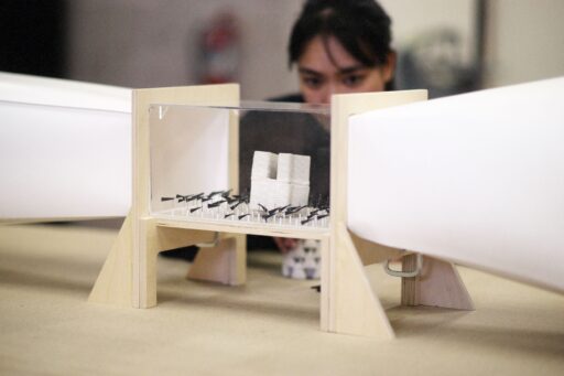 A student peering at a small architectural model on a wooden stand