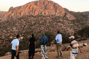 A group of people on the job, observing the landscape during a field visit with a rocky mountain in the background.