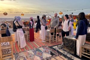 Students chatting on Berber - style rugs around rattan chairs at sunset