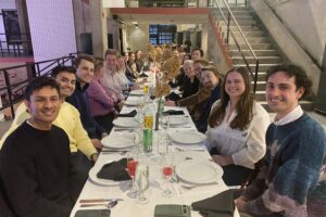 Students seated at a long, decorated dinner table set with wine glasses and black napkins