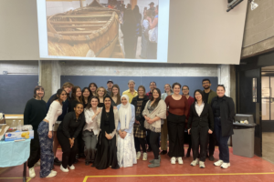 Group photo of students, faculty, and community members in front of a projected image of a traditional canoe in a studio.