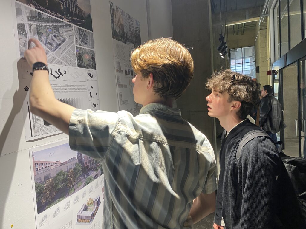 People looking at posters on the wall and models.