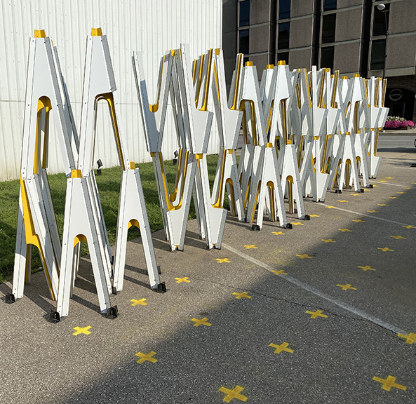 Zigzagging white and yellow folding metal structures arranged on pavement marked with yellow crosses.