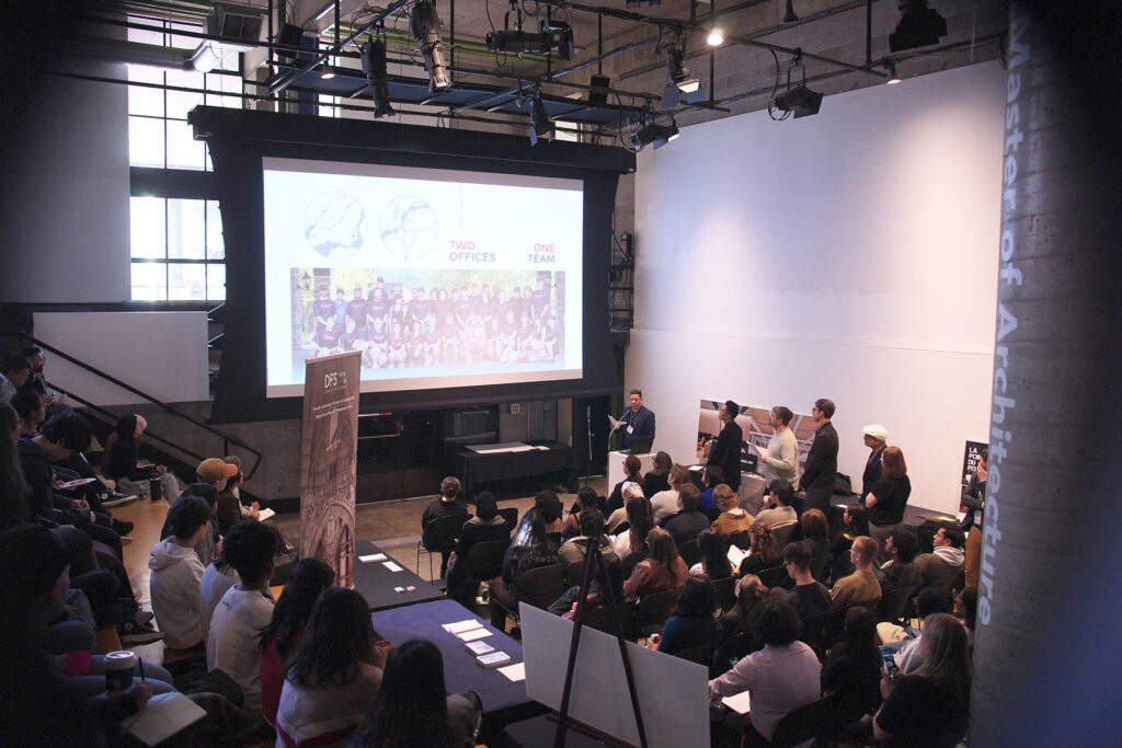 Audience seated in The Pit listening to a speaker presenting slides at the Shop | Talk Career Fair event.