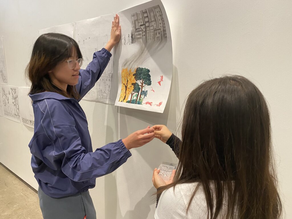 Two students pin up a drawing on the wall