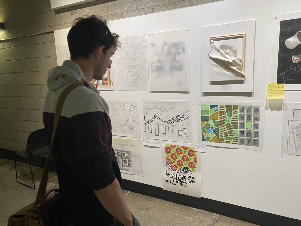 Student viewing a wall of drawings and mixed-media artworks pinned up for exhibition.