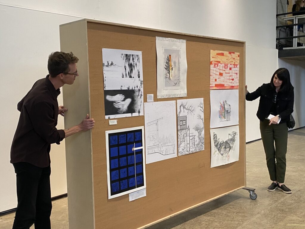 Two people stand on either side of a board displaying winners’ drawings from the Murray & Murray Competition.