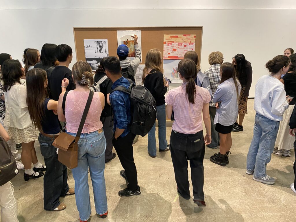 A group of students gathers around a display board showing the winning drawings of the Murray & Murray Competition.