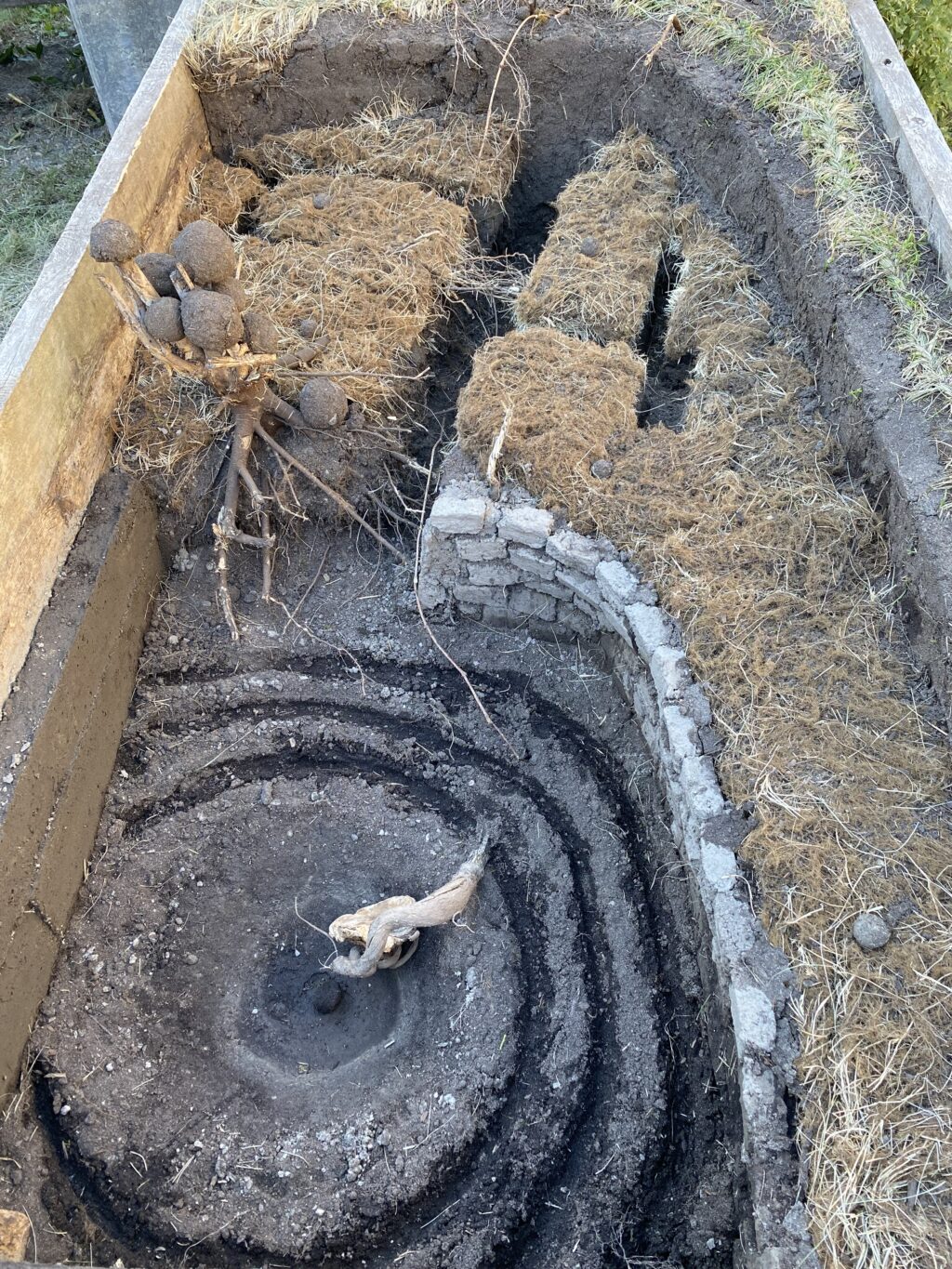 Carved concentric circles in soil with raised wall, rectangular turf blocks, and stacked earth balls on branches.