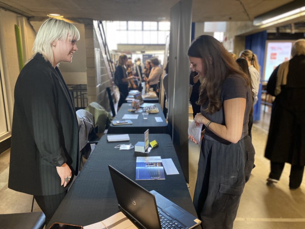 Student speaking with an employer across a booth table at the Shop | Talk Career Fair
