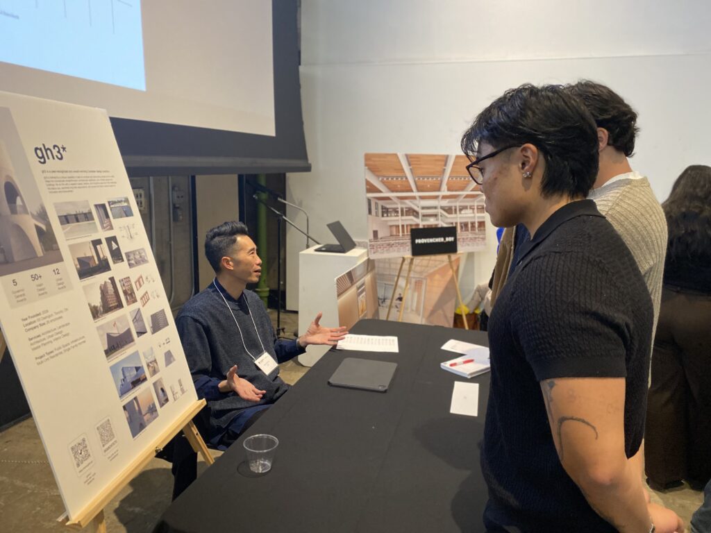 Students speaking with an employer at a career fair booth with architectural display boards.