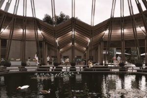 A rendering of people seated inside a timber pavilion over a shallow pond.