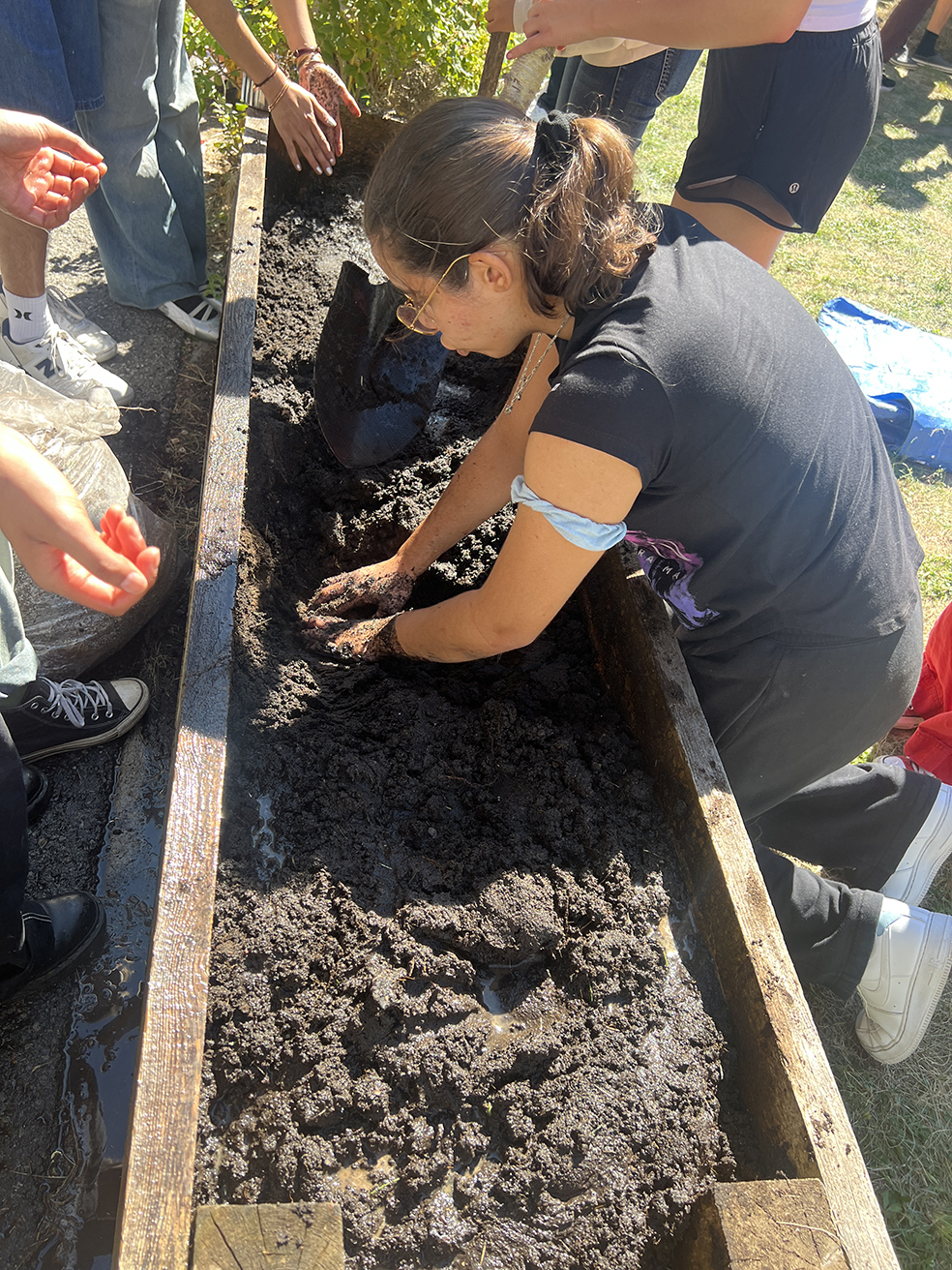 Students shaping wet soil by hand inside a planter