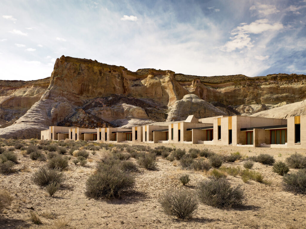 Long, low-lying building in desert landscape with layered rock cliffs rising steeply behind it