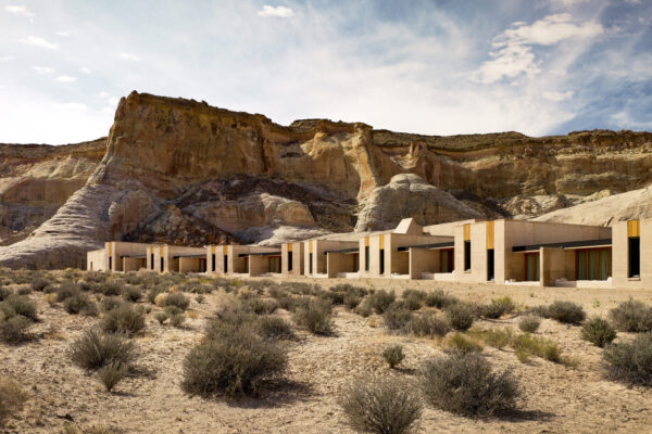 Long, low-lying building in desert landscape with layered rock cliffs rising steeply behind it