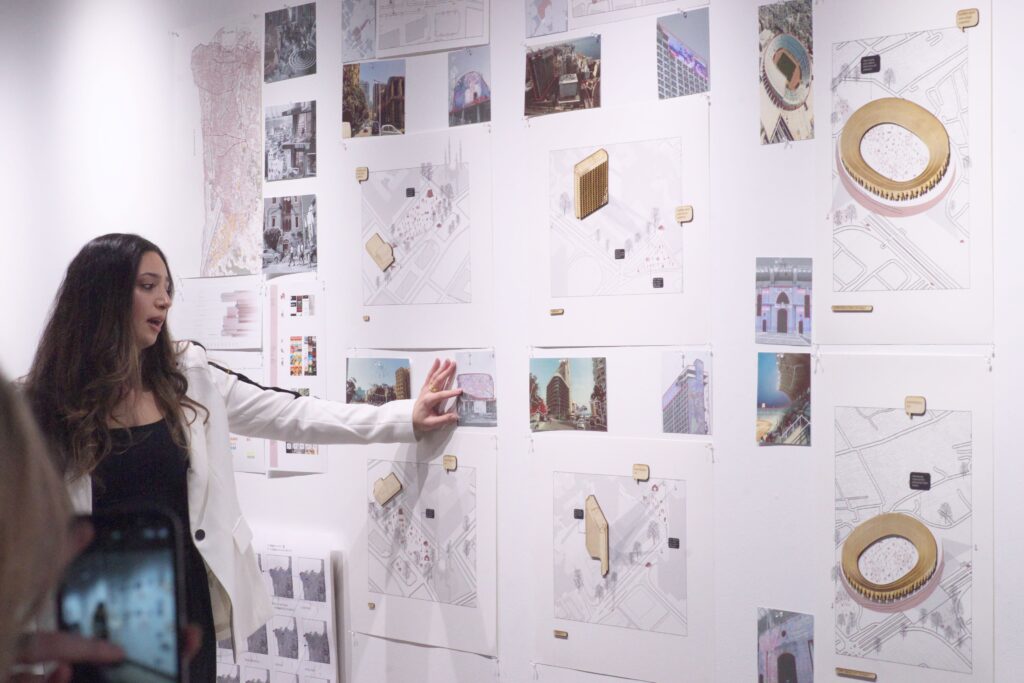 Student presenting architectural drawings and renderings pinned on a white wall during a critique
