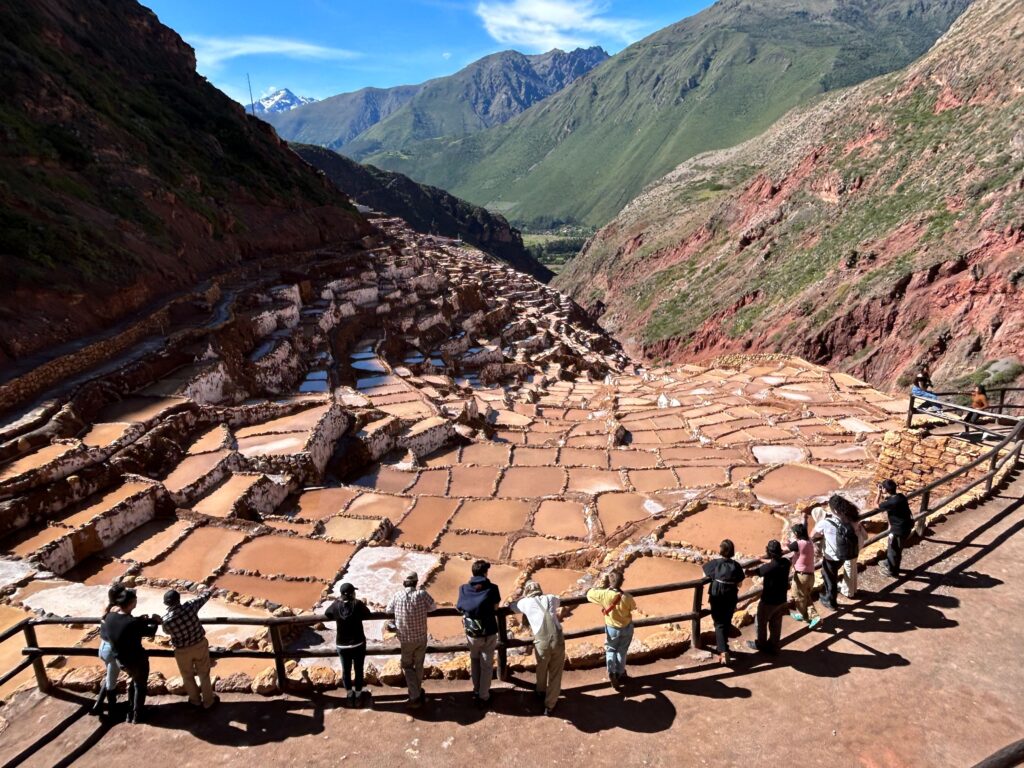 Group of students standing at a railing overlooking terraced salt ponds set in a mountain valley during a travel studio.