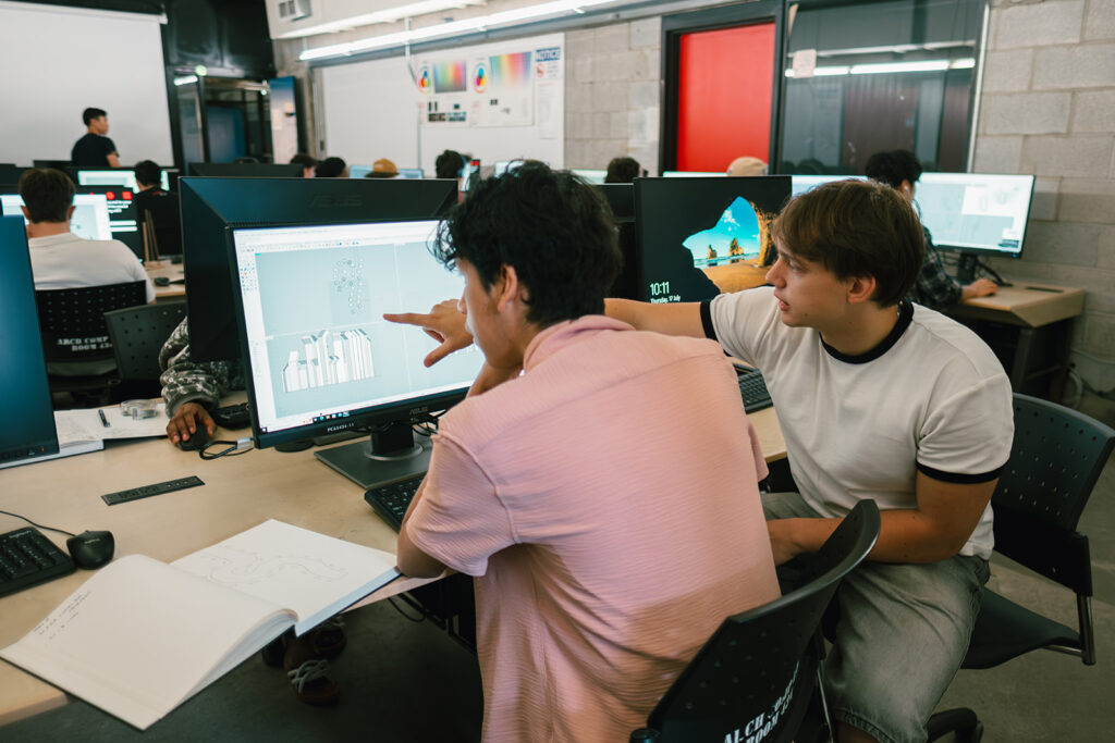 Student pointing at a 3D model in Rhino while discussing with a peer in a computer lab.