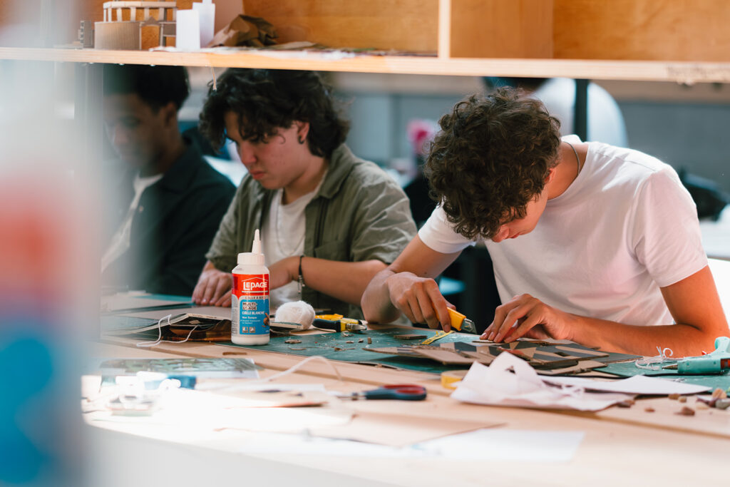 Student using a utility knife to cut cardboard while another student works beside
