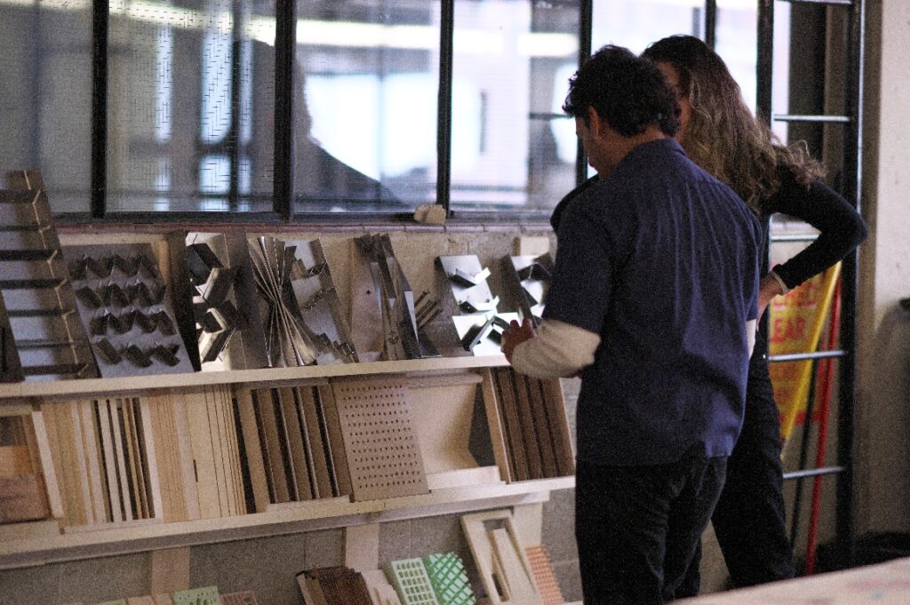 Two people standing in front of a wall of material samples, discussing the displayed pieces