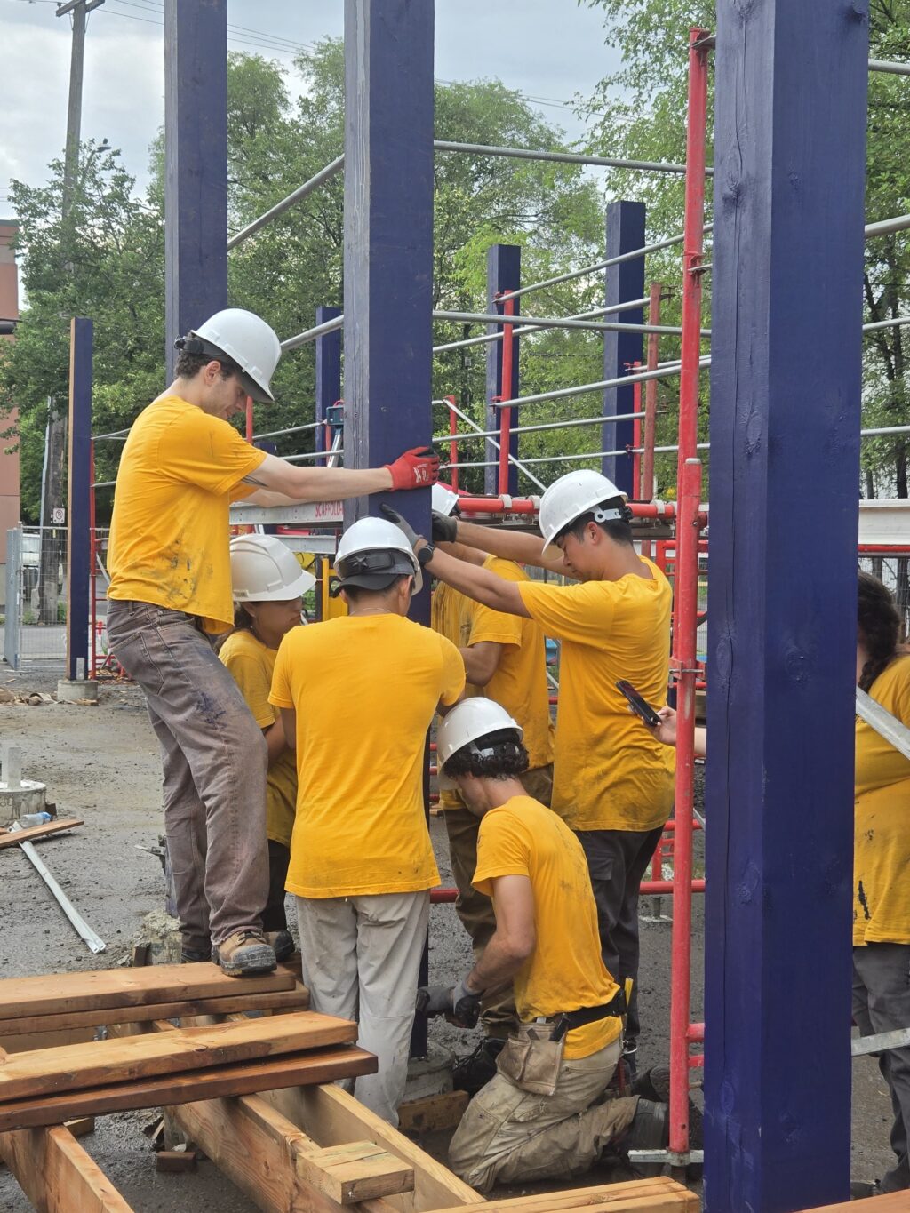 Team installing a blue structural post using scaffolding during construction at Vanier Hub.