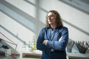 Billy Fleming with long curly hair and glasses standing with arms crossed