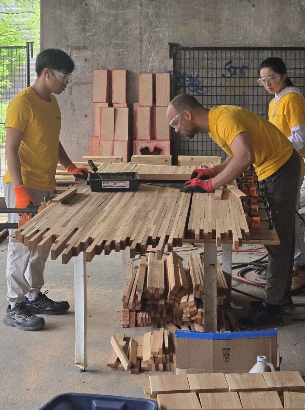 Team measuring and assembling wooden slats on a worktable during fabrication.