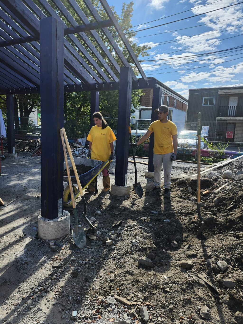 Students preparing the ground around blue structural posts during construction.