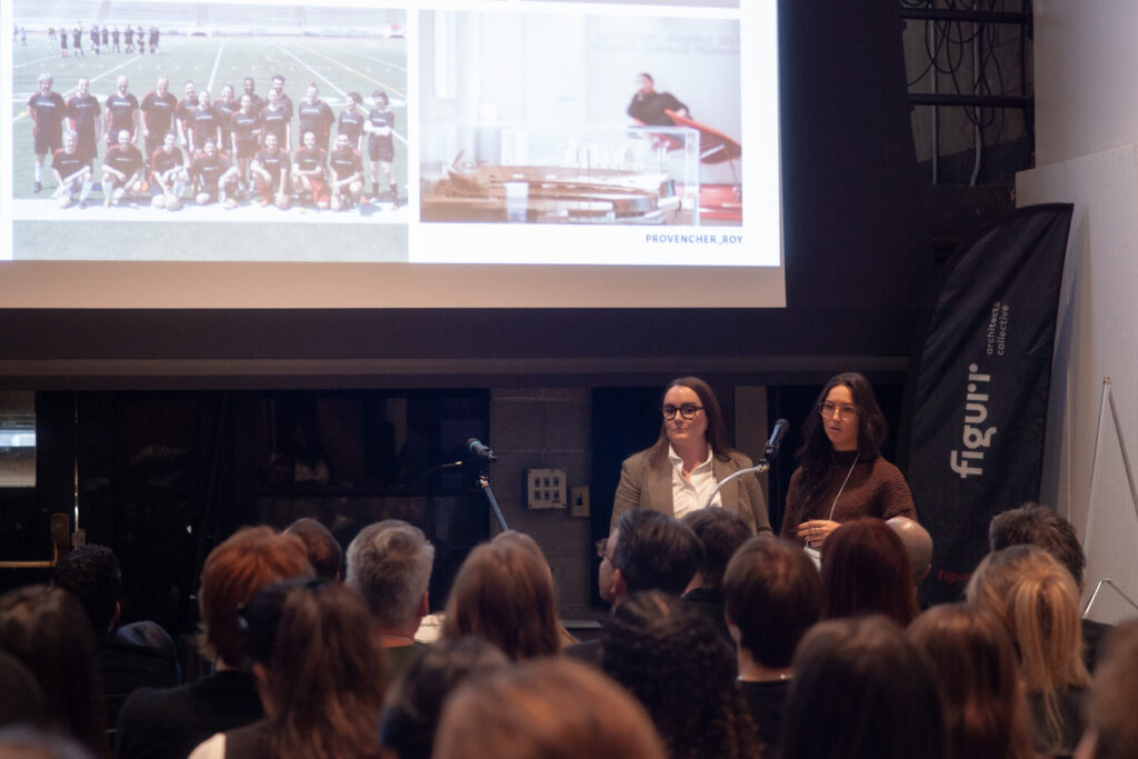 Two women stand on stage giving a presentation at a career fair event with a projected screen behind them.