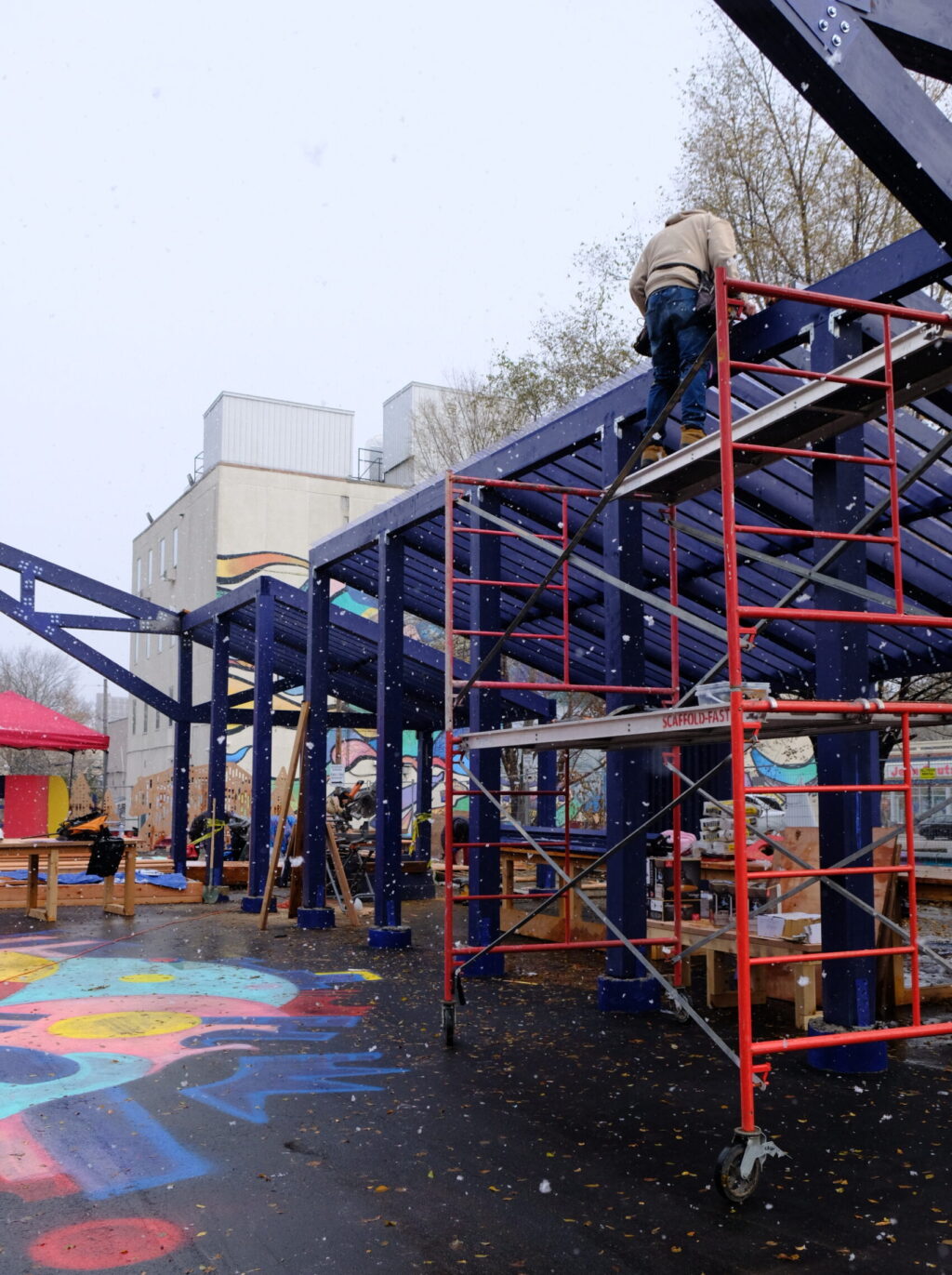 Scaffolding set up beside a blue frame structure during snowy construction work.