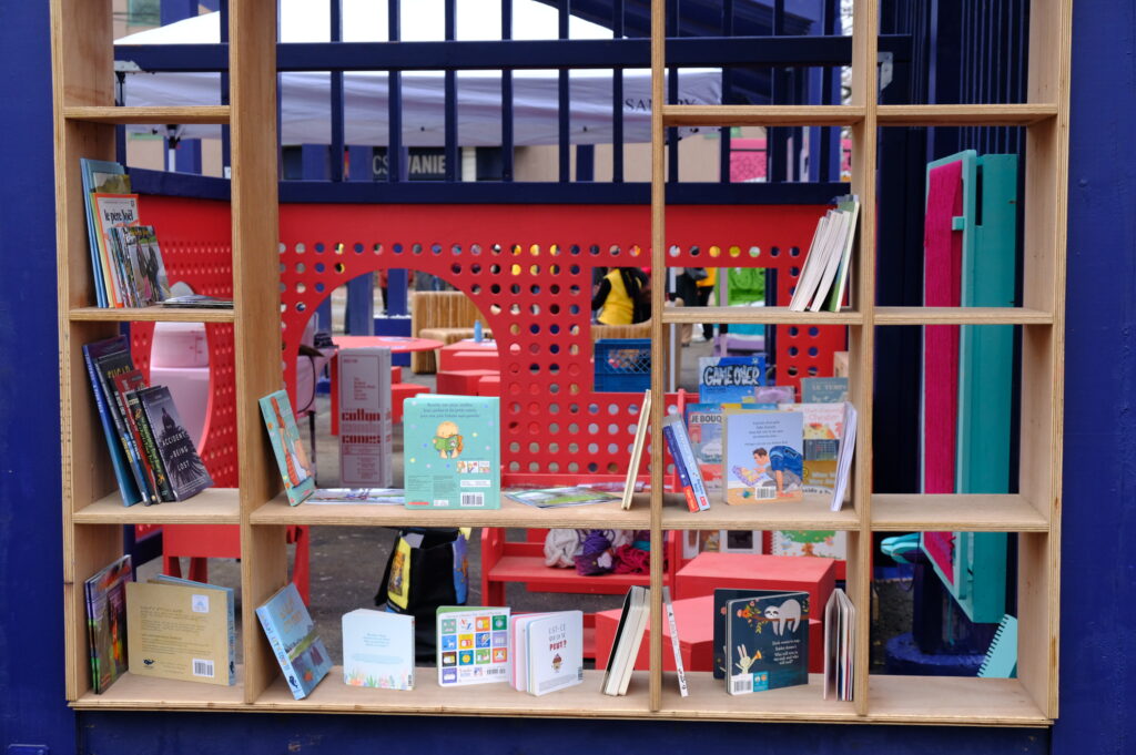 Wooden shelving filled with children’s books beside the red play structure at Vanier Hub.