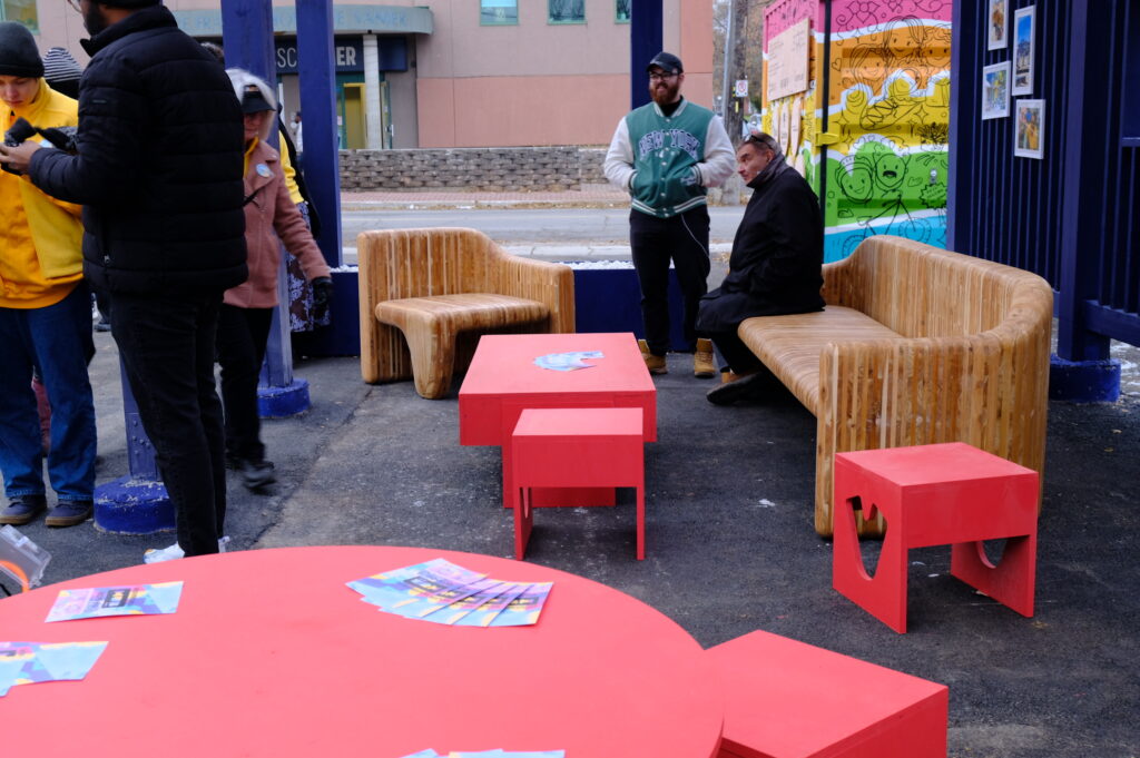 People gathering around the student-built seating area with wood benches and red tables at the Vanier HUB.