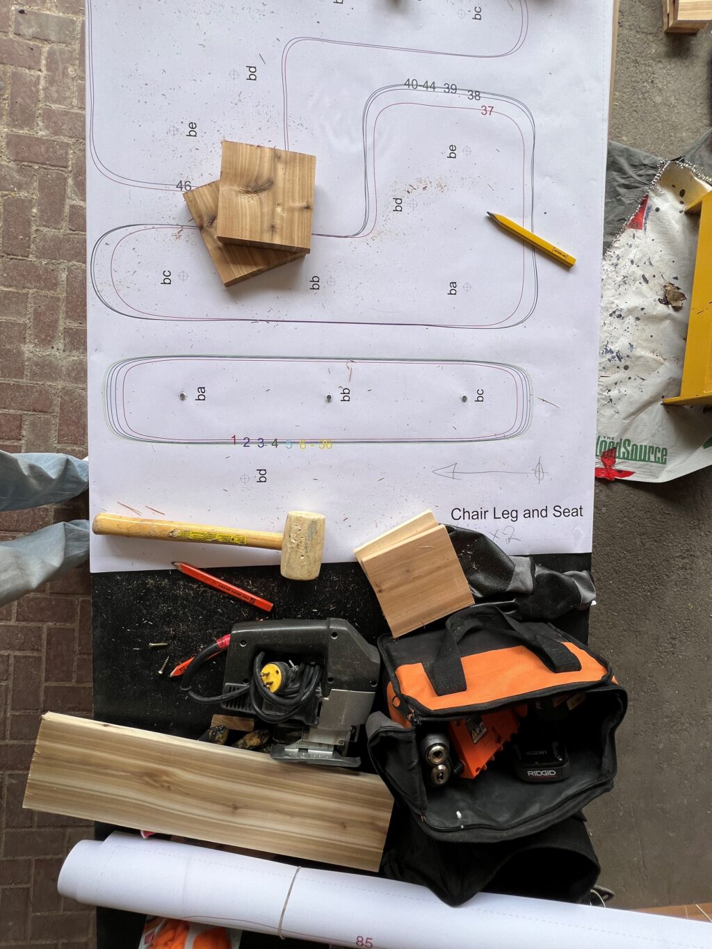 Pattern sheet with chair outlines surrounded by wooden pieces and tools used for furniture making.