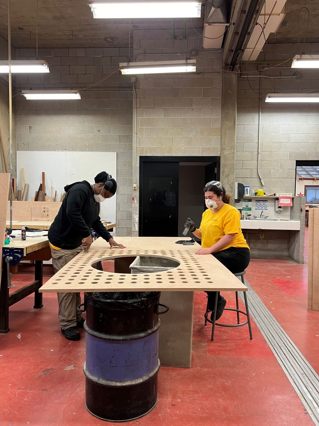 Students sanding and finishing a perforated plywood panel in the workshop for the HUB structures