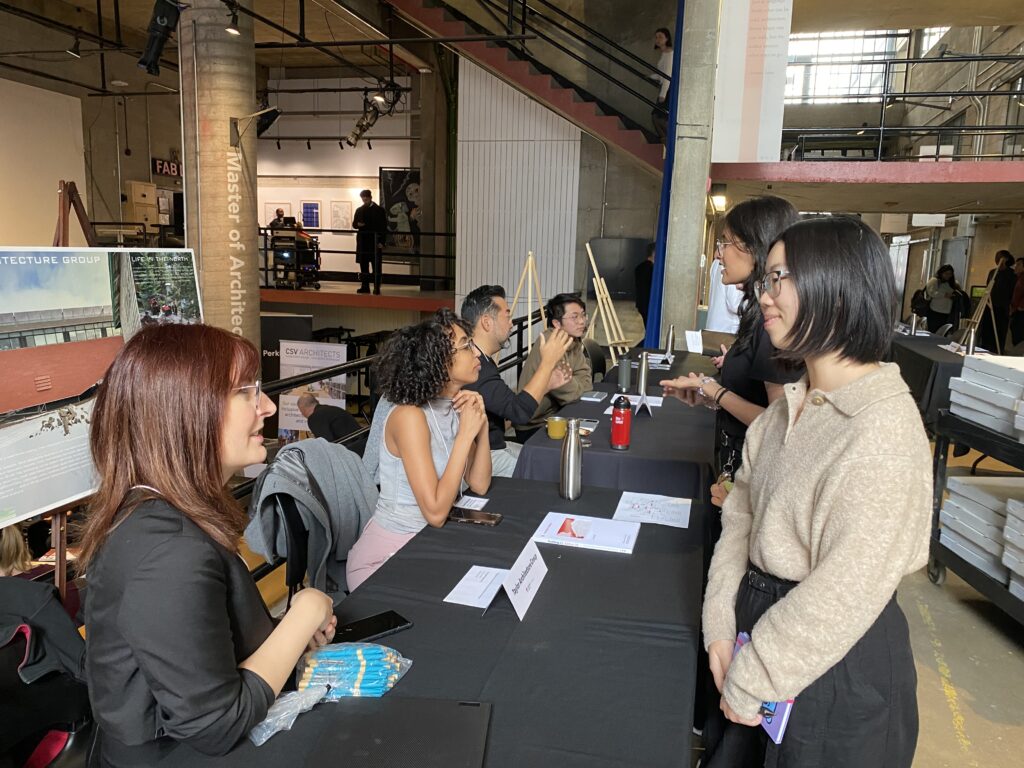 Architecture students speak with Taylor Architecture Group representatives seated behind tables.