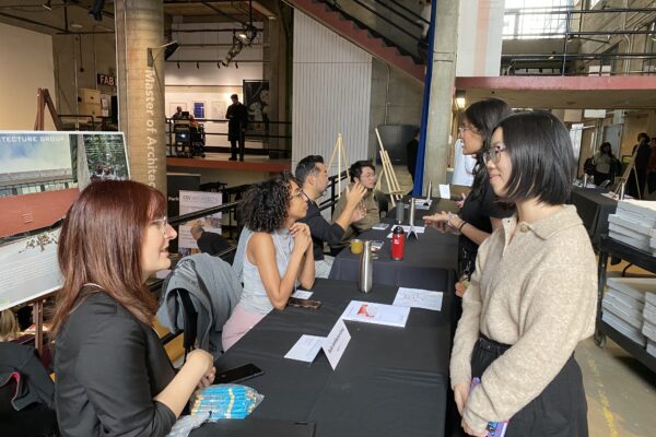Architecture students speak with Taylor Architecture Group representatives seated behind tables.