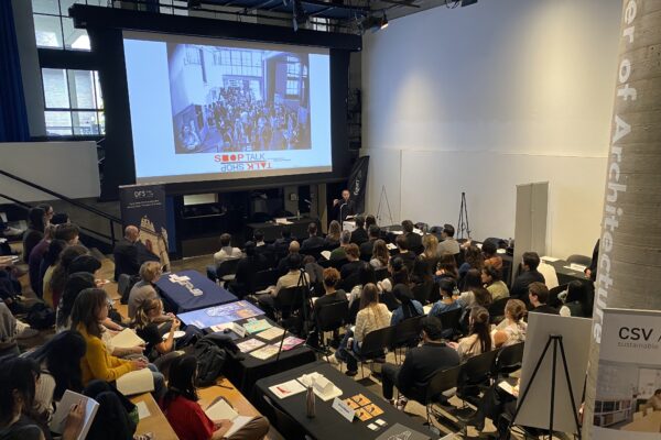 Wide view of a packed auditorium during a Shop Talk lecture, with posters and booths visible around the Pit.