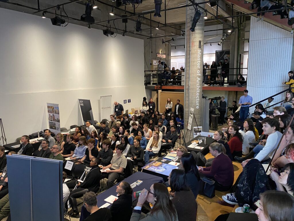 Crowded event space with students seated and professionals presenting during the Shop Talk career fair.