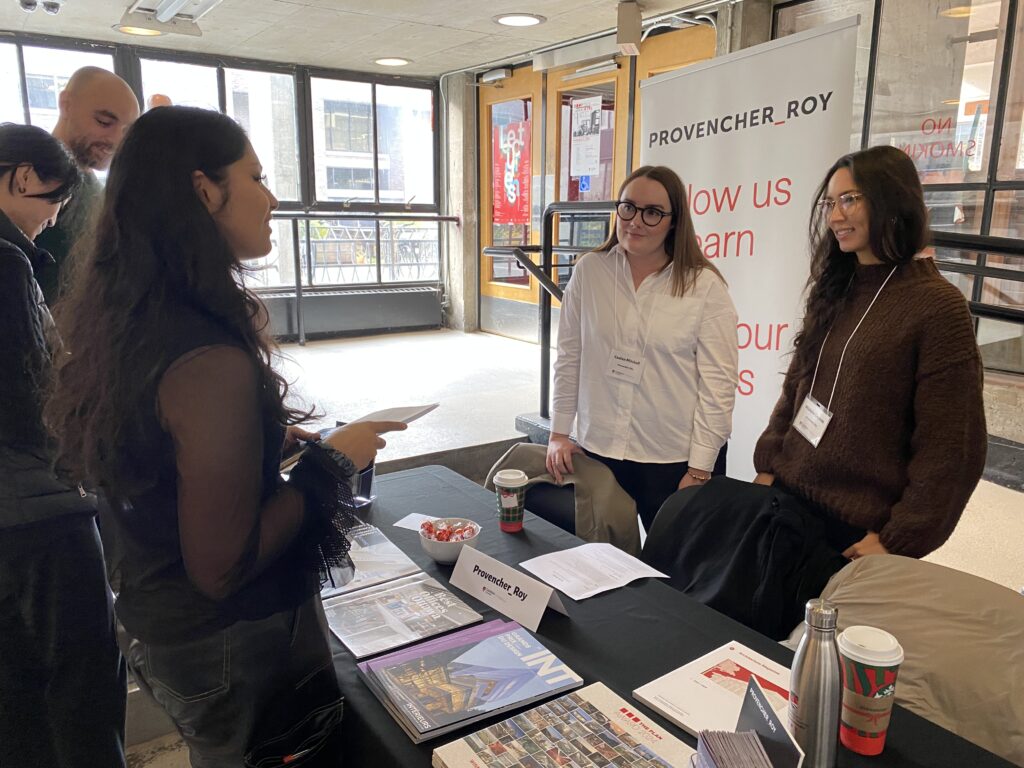 Student speaks to a Provencher_Roy representative at her career fair table, with brochures and signage displayed.