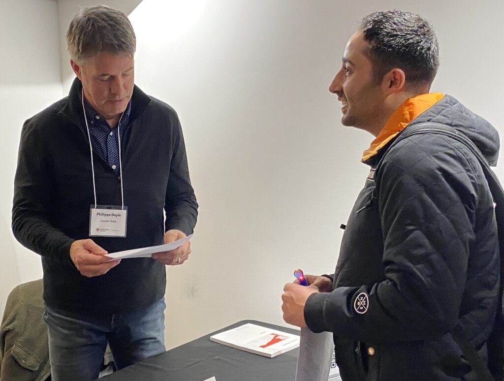 Philippe Doyle looks at a document while speaking with a student at the Lalande + Doyle table