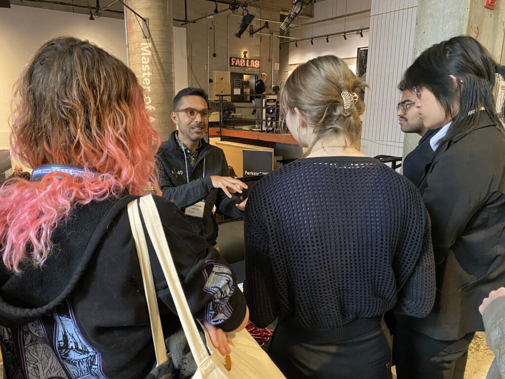 A firm representative speaks to a line of students holding notebooks and listening attentively.