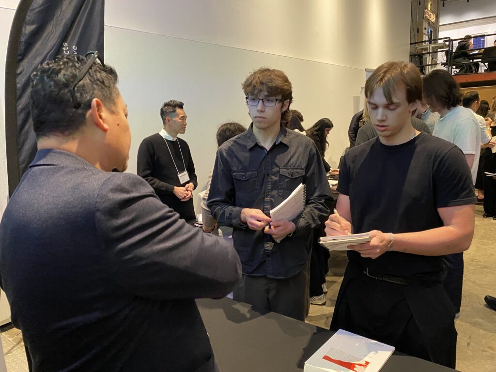 Roberto Campos talks with two students holding notebooks