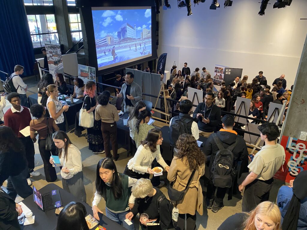 Wide view of a busy career fair, showing booths, banners, and crowds of students and firm representatives.