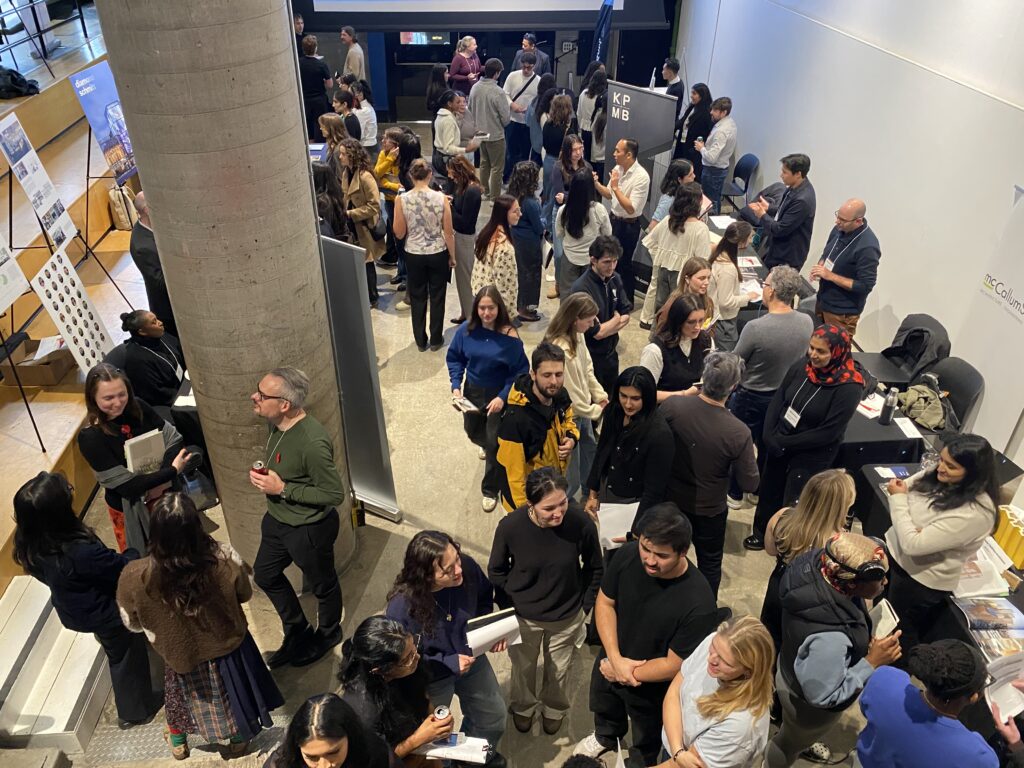 A busy career fair floor with students and firm representatives engaged in conversation at multiple tables.
